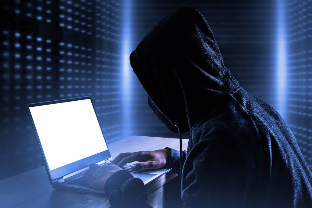 A person in a black hoodie using a laptop, symbolizing a data breach exposing individuals' personal information